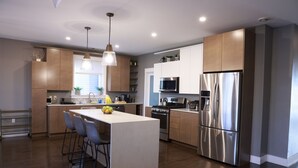 Une cuisine moderne dotée d’un îlot central, d’appareils électroménagers en acier inoxydable et d’un luminaire suspendu.