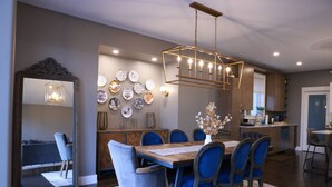 Un coin repas avec une table en bois, des chaises à l’assise rembourrée de tissu bleu et un luminaire suspendu.