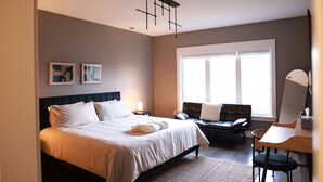 Une chambre d’hôtel moderne équipée d’un grand lit, d’un bureau, d’une chaise et d’une fenêtre laissant entrer la lumière naturelle.