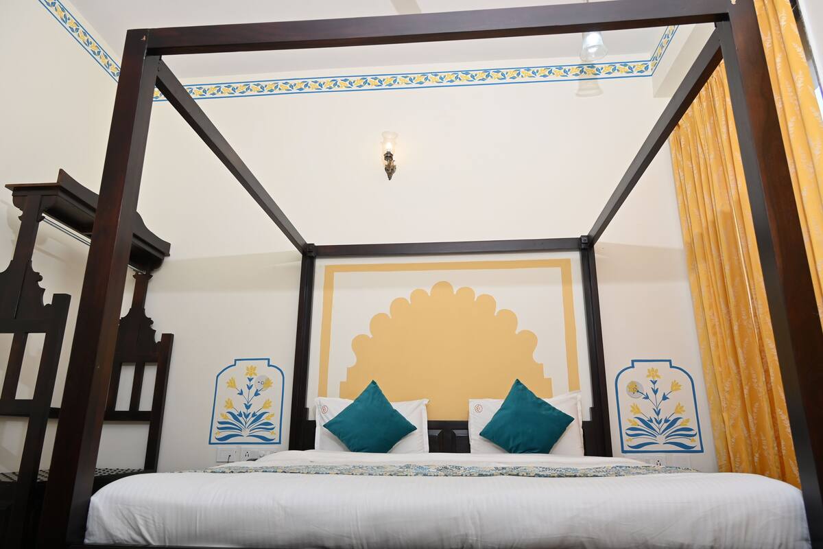 Ein Bett mit Baldachin und einem dekorativen Kopfteil, eine Wand mit floralem Muster und eine Deckenleuchte.