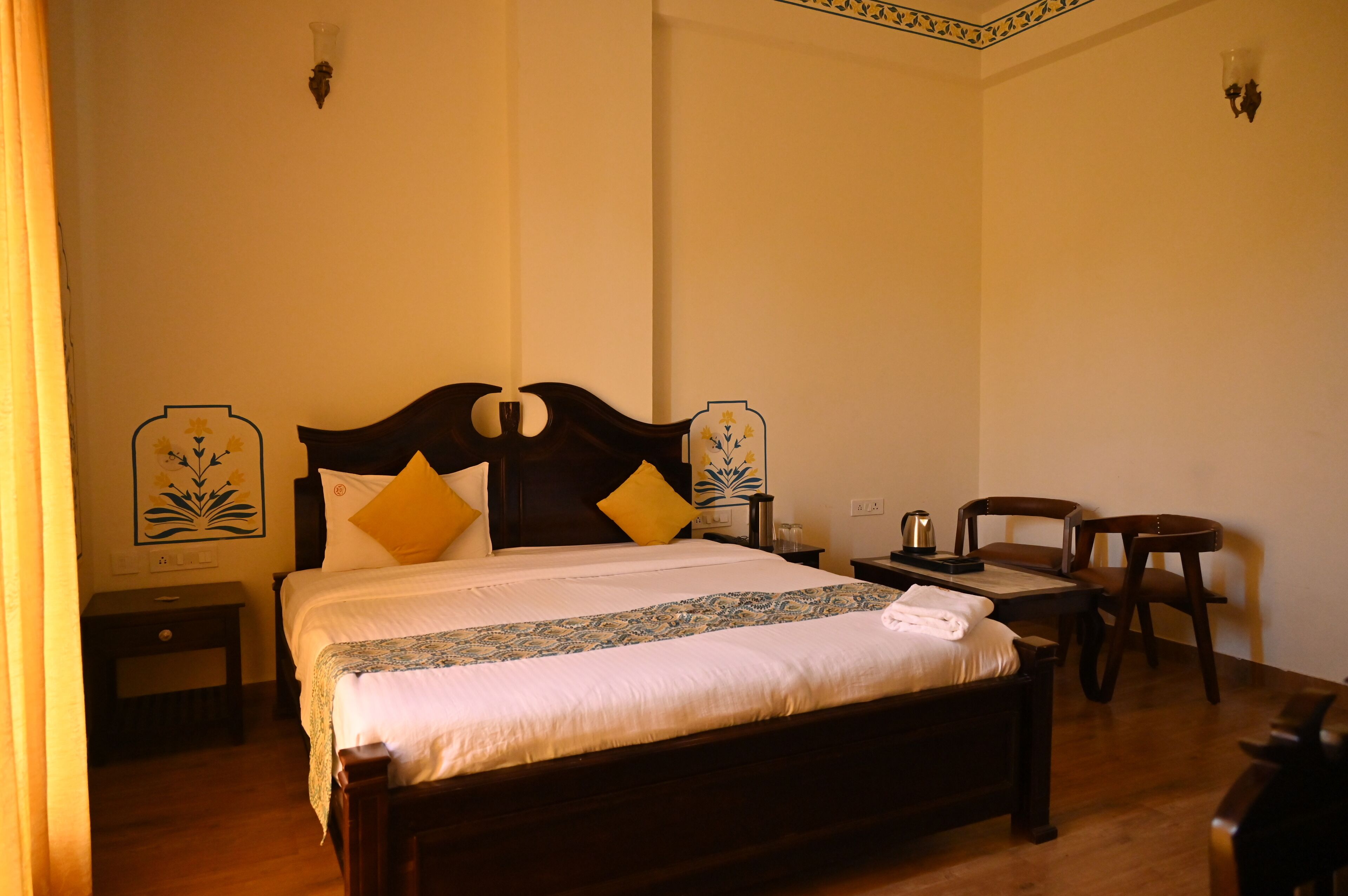 A neatly made bed with a wooden headboard, two bedside tables, and a small table with a kettle.
