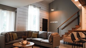 A modern living room with a sectional sofa, a round coffee table, and a staircase with wooden railings. - Apartment on Broadway St - L (Sugarcreek)