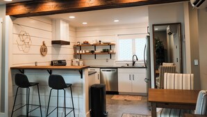 A modern kitchen with a wooden island, bar stools, a dishwasher, and a dining area with striped chairs. - Apartment on Broadway St - L (Sugarcreek)