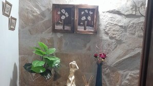 A stone wall with framed pictures, a wooden console table with a statue, a potted plant, and a vase with flowers.