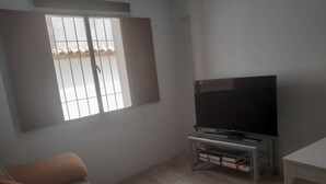 A living room with a sofa, a TV on a stand, and a window with bars.