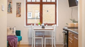 Eine Küche mit großem Fenster, einem Esstisch mit Stühlen, einem türkisfarbenen Sofa und einer Küchenzeile mit Geräten.