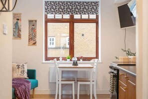 Une cuisine dotée d’une grande fenêtre, une table à manger avec des chaises, un canapé de couleur turquoise et un comptoir de cuisine équipé d’appareils électroménagers.