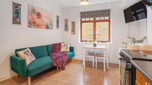 Ein gemütlicher Wohnraum mit einem grünen Sofa, einem Esstisch mit Stühlen, einer Küchenzeile und Bildern an den Wänden.