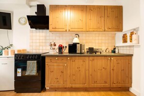 A kitchen with wooden cabinets, a stove, a microwave, and a kettle.
