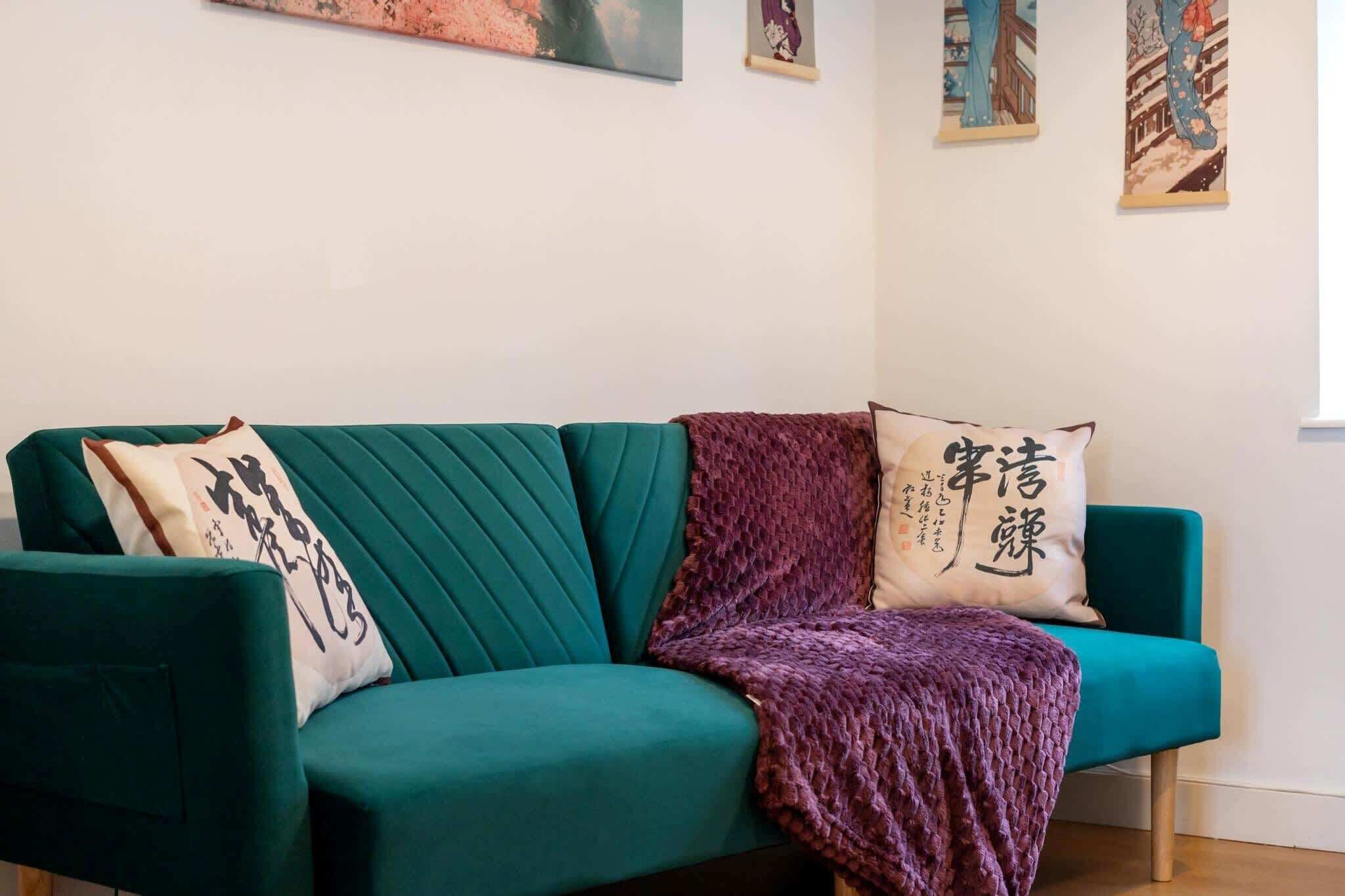 A teal sofa with two decorative pillows and a purple throw blanket.
