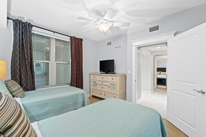 Ein Schlafzimmer mit zwei Betten, einem Deckenventilator, einem Fernseher auf einer Kommode und einer Tür zu einem anderen Raum.