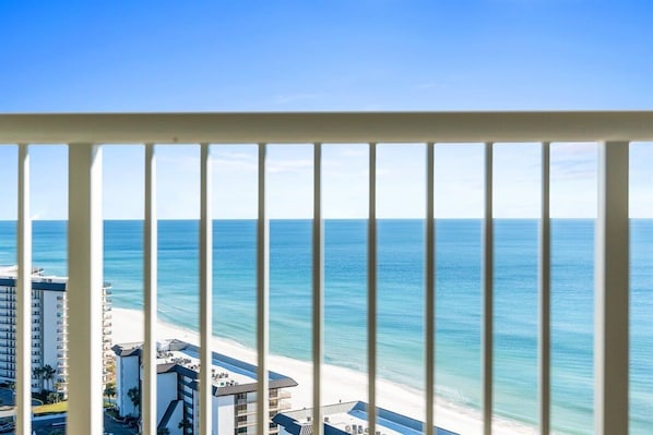 Blick von einem Balkon mit Geländer auf Strand und Gebäude, bewölkter Himmel.