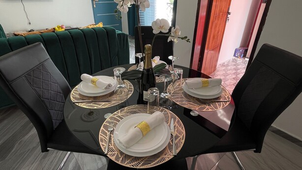 A dining table set for three with a bottle of champagne, glasses, and plates. - RESIDENCE HMR Douala - Lendi (Douala)