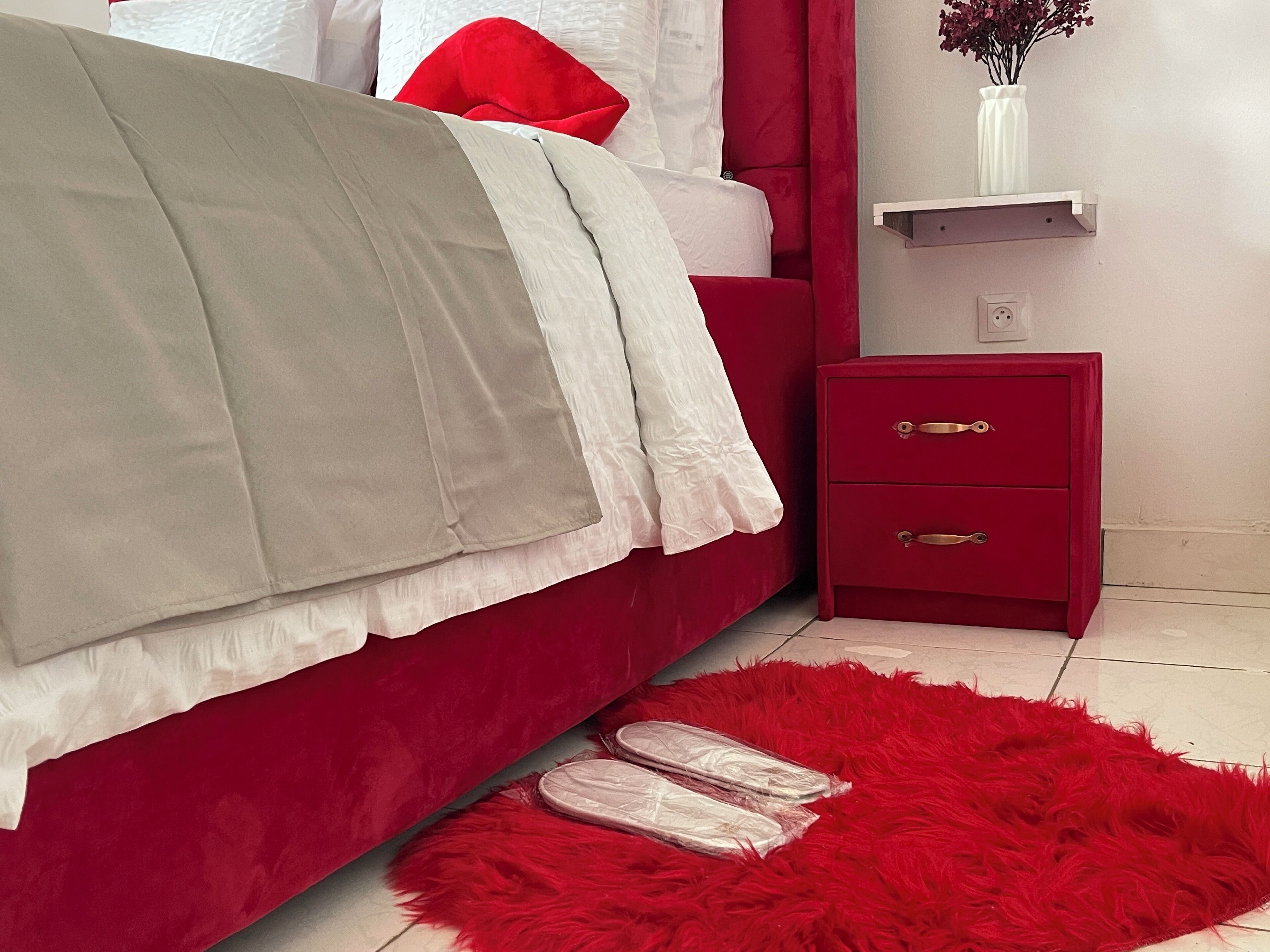 Ein Schlafzimmer mit einem roten Bett, einem roten Nachttisch und einem roten, flauschigen Teppich.