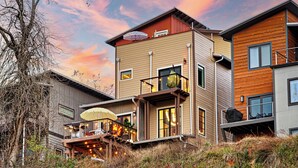 Een modern meerlaags huis met een balkon, een overdekte zitplaats buiten en een trap naar de bovenverdieping.