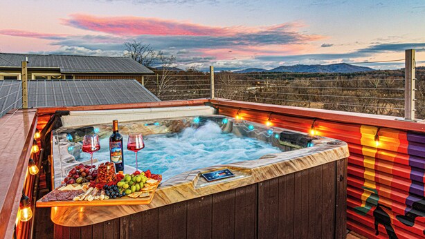 Een hottub met een houten terras, omringd door een houten hek, en een prachtig uitzicht op bergen in de verte.