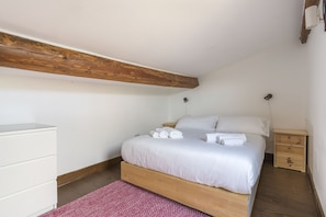 A bedroom with a wooden bed frame, white bedding, a white dresser, and a wooden nightstand with a lamp. - Fiesolana 27 Glass in Firenze (Florence)