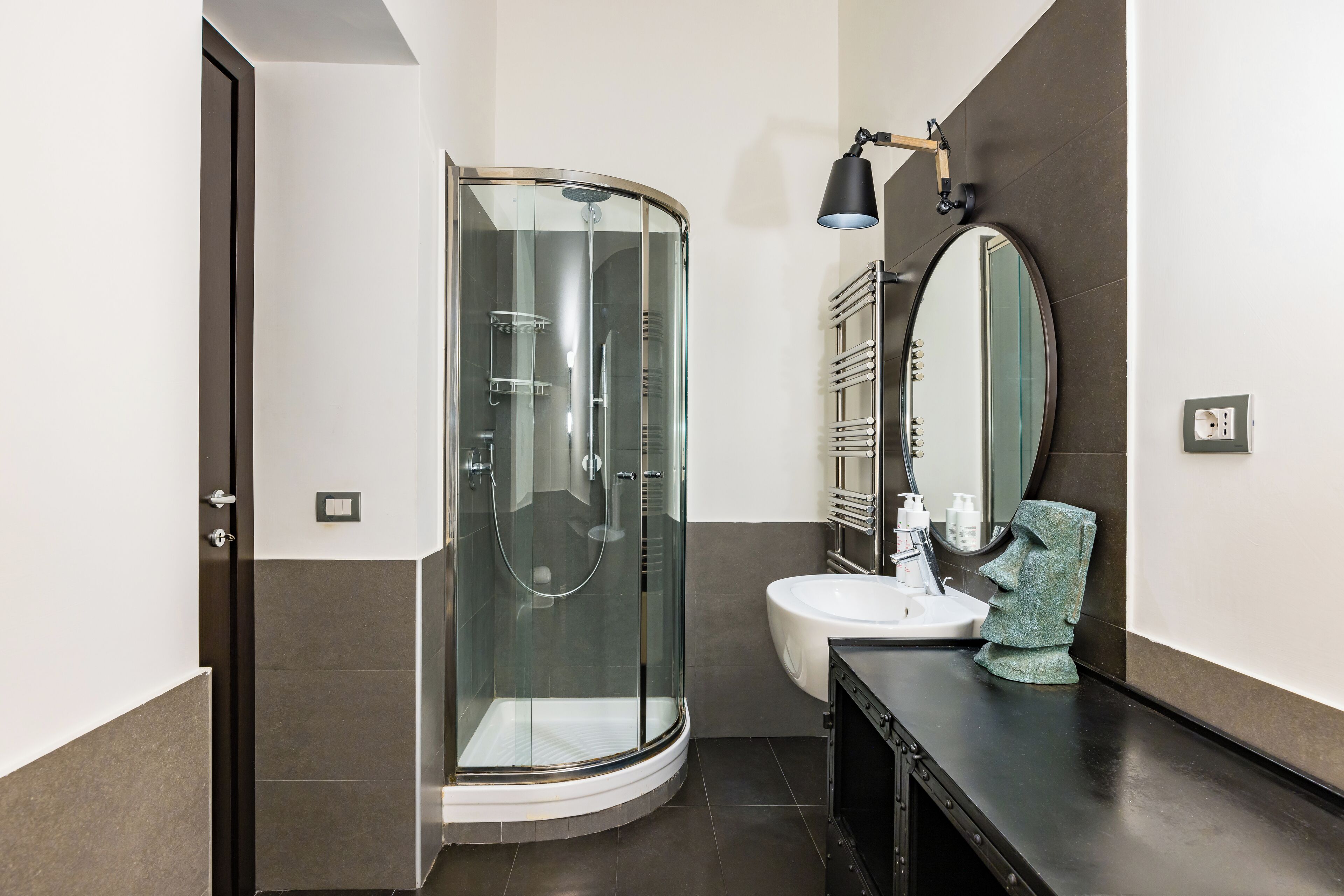 Un baño moderno con ducha de vidrio, lavabo y tocador con espejo y perchero para toallas.