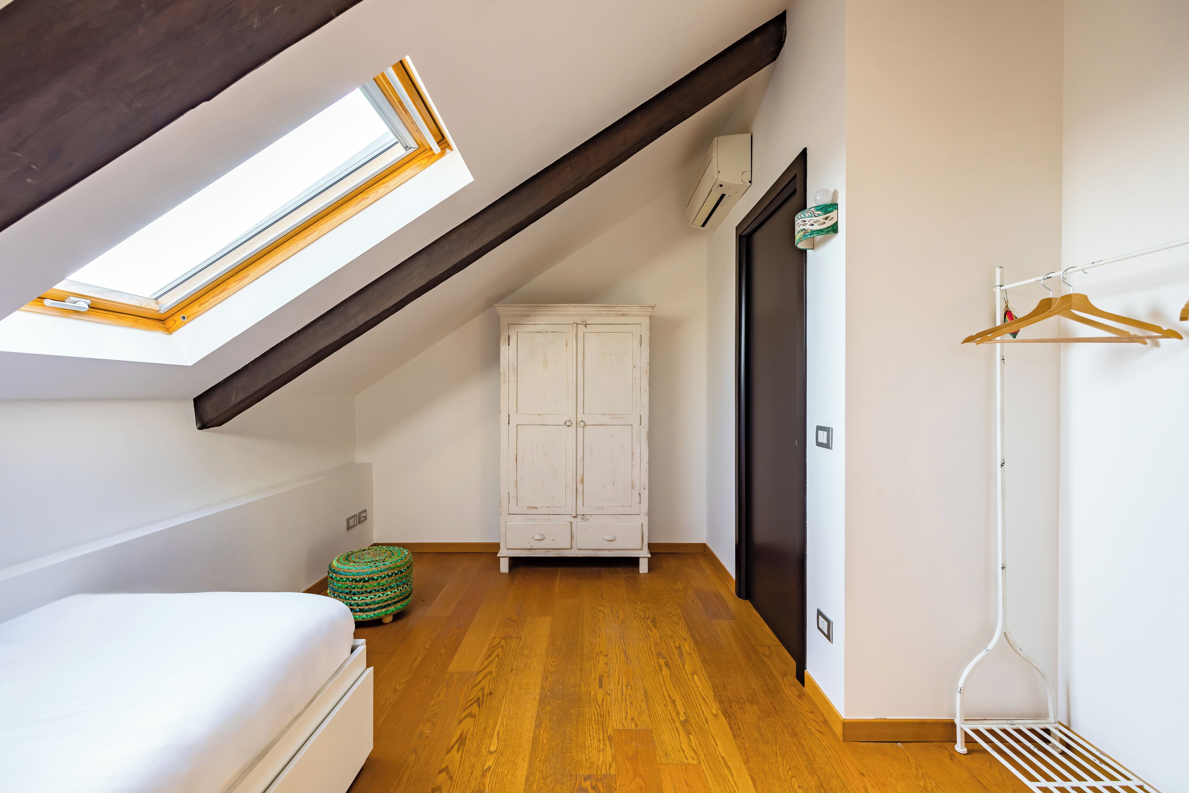 A room with a sloped ceiling, a skylight, a white wardrobe, a wooden floor, and a clothes rack.