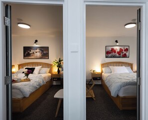 Une chambre d’hôtel avec deux lits, une tête de lit en bois, une table de chevet avec une lampe, une petite table sur laquelle est posé un vase de fleurs, et un tableau accroché au mur.
