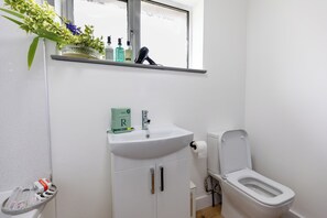 Une salle de bain avec un lavabo blanc, des toilettes et une fenêtre située au-dessus du lavabo.