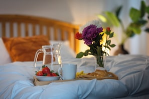 A neatly made bed with a tray of breakfast items including strawberries, a pitcher of water, a mug, and a small vase with flowers. - Norwich - House - Sleeps 7 - Parking - Garden (Norwich)