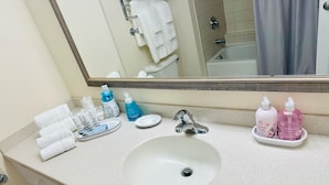 Un baño con lavamanos blanco, un espejo y artículos de tocador en la encimera.