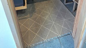 Una sala de sauna con bancos de madera, un banco con asiento negro y suelo perforado.