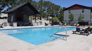 A swimming pool with a lounge area, a covered seating area, and a building with a red roof.