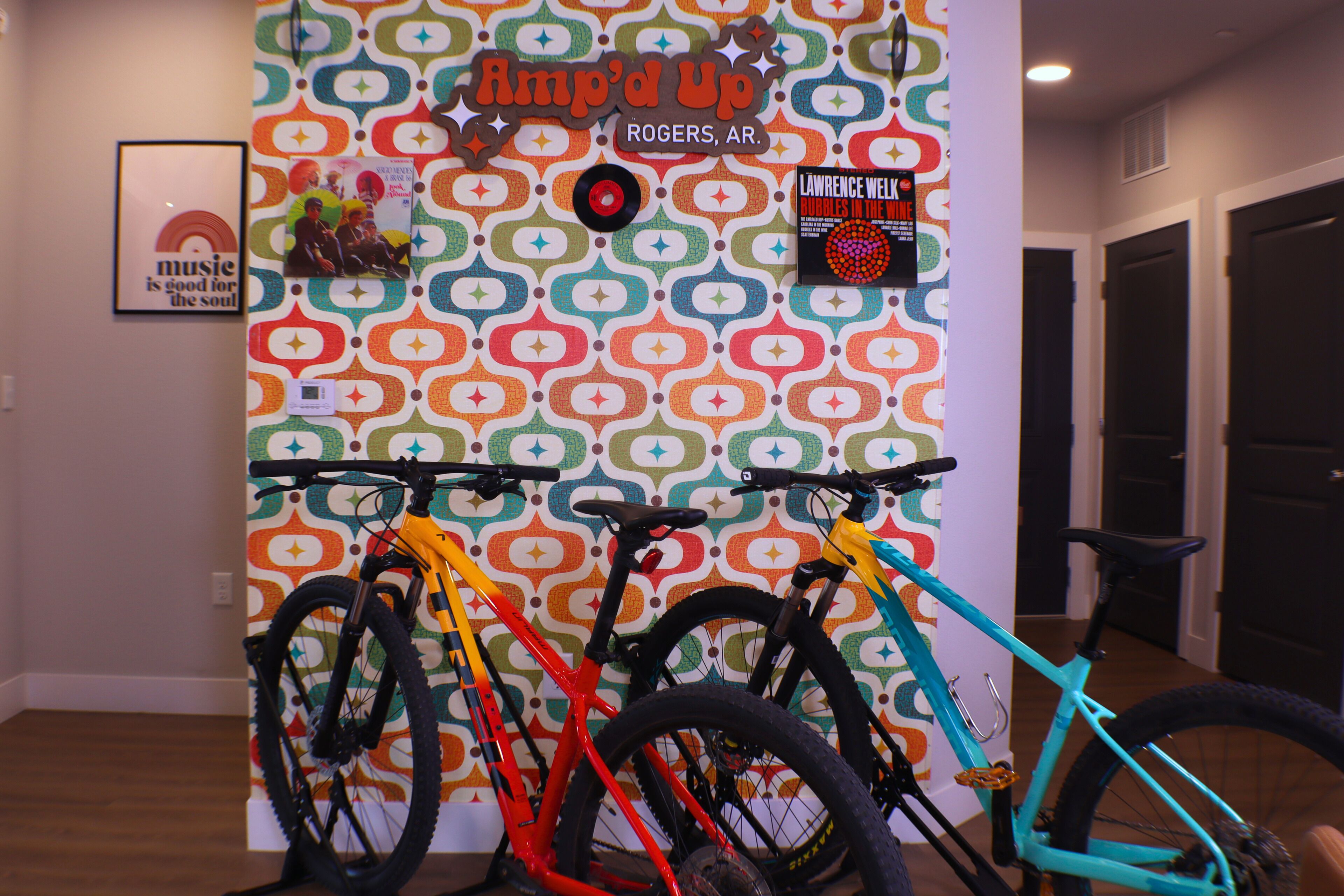 A room with a colorful patterned wall, a framed picture, and three bicycles.
