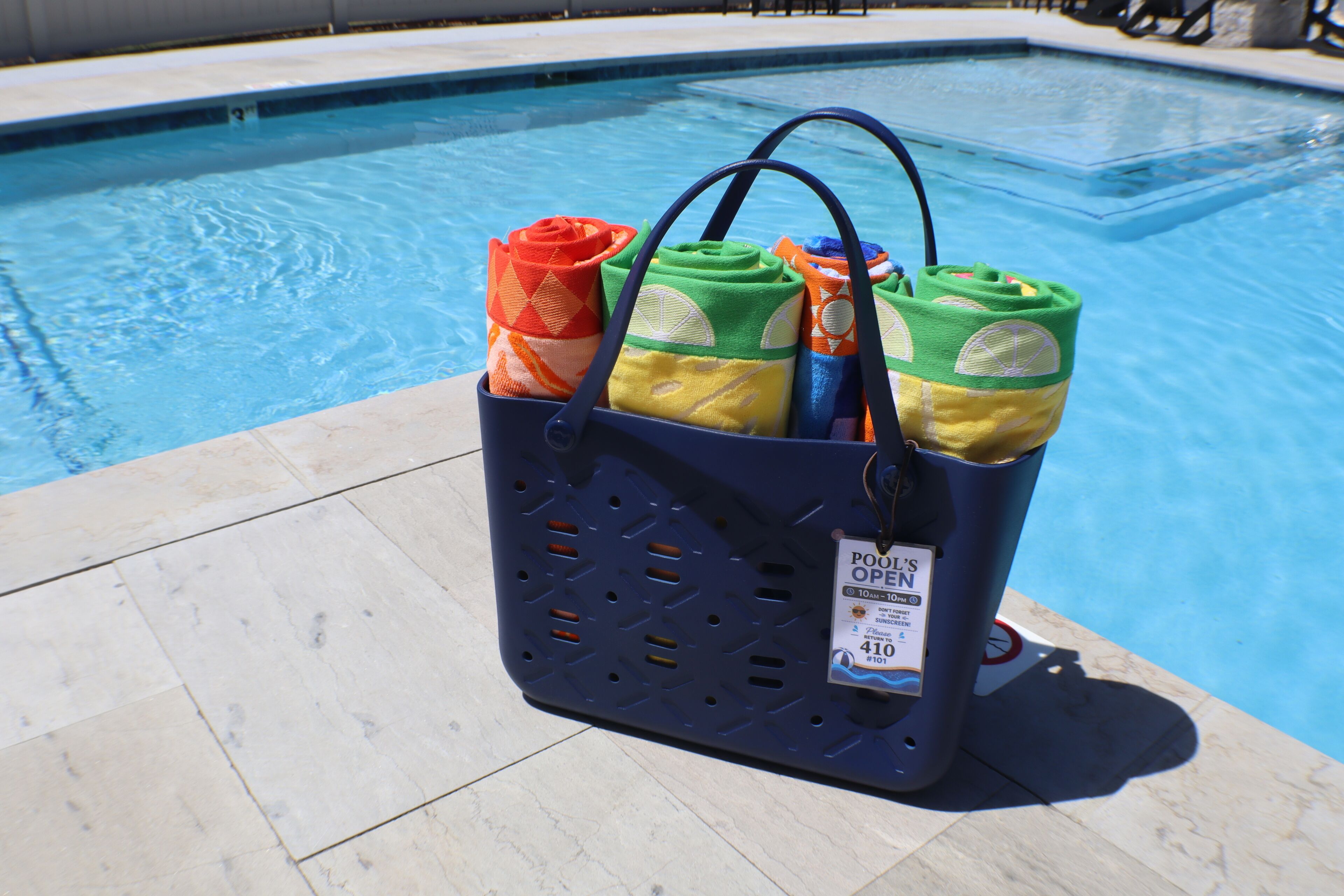 A poolside setting with a blue pool, a poolside chair, and a blue basket with towels.