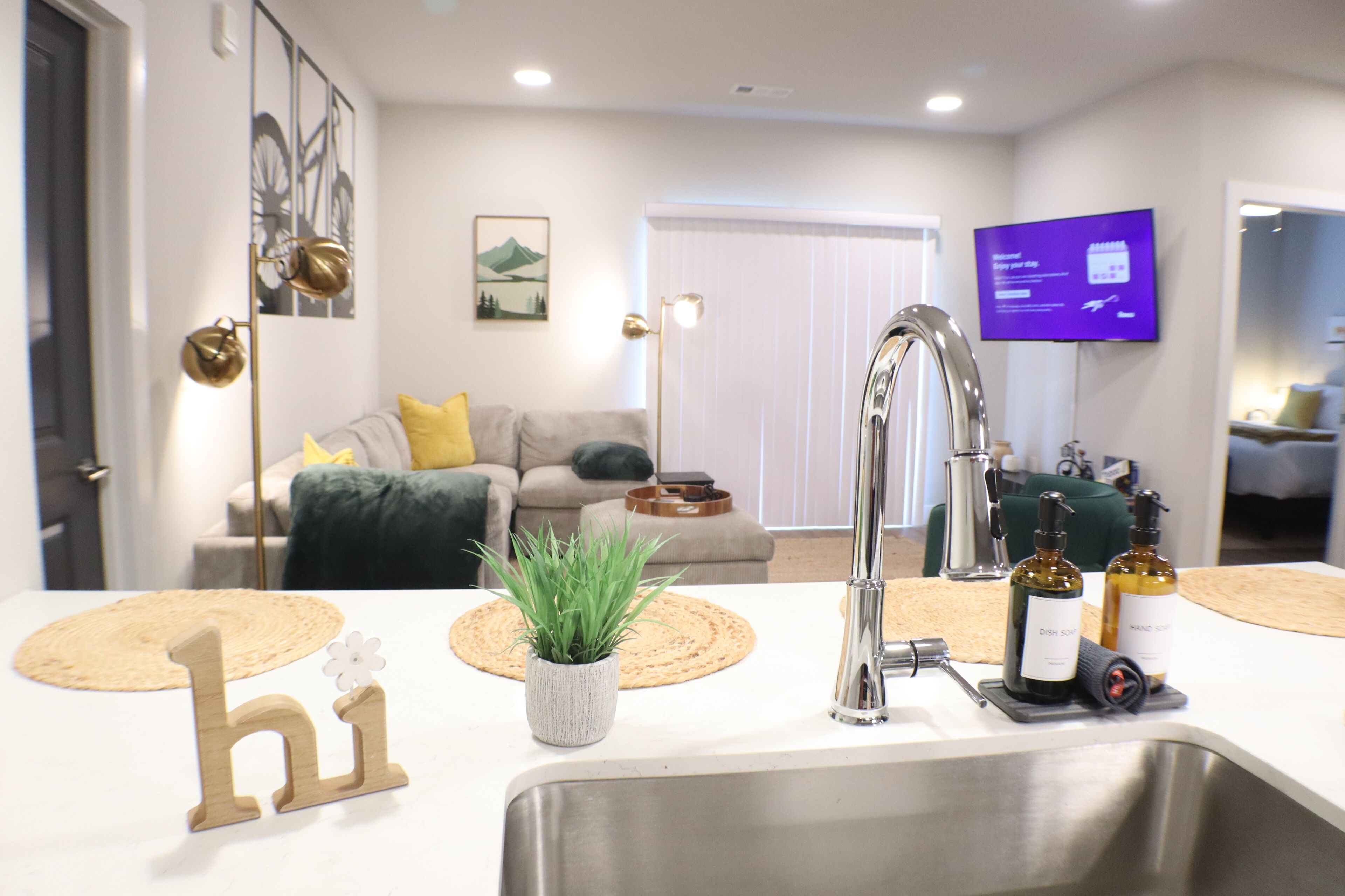 A modern kitchen with a stainless steel sink, a potted plant, and a 'hi' sign.