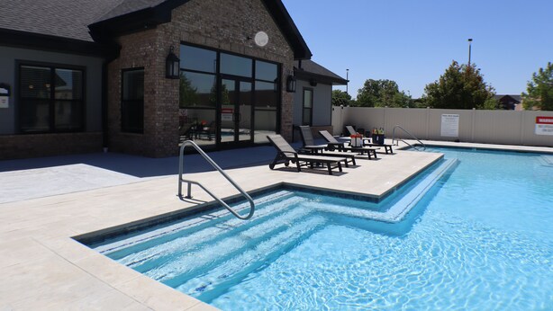 A swimming pool with lounge chairs and a building with large windows. - Deluxe 2BR with king suites & pool near the Walmart NWA Championship. (Rogers)