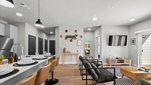 A modern kitchen with a central island, black chairs, and a dining area with a black and white striped rug. - Music-Inspired 2BR | King Suites, Pool & Near AMP (Rogers)