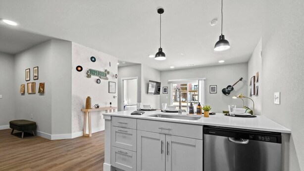 A modern kitchen with white cabinetry, a stainless steel dishwasher, pendant lighting, and a wooden bench. - Music-Inspired 2BR | King Suites, Pool & Near AMP (Rogers)