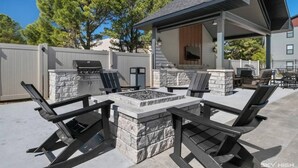 An outdoor patio with a stone fire pit, seating, and a grill. - Music-Inspired 2BR | King Suites, Pool & Near AMP (Rogers)