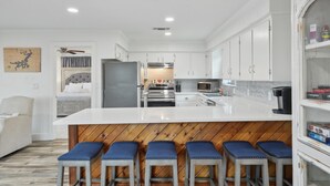 Une cuisine moderne avec des meubles blancs, un îlot central doté de tabourets de bar et une vue sur la chambre adjacente.