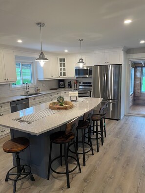 A modern kitchen with white cabinets, stainless steel appliances, and a large island with bar stools. -  Quaint and cozy cottage like atmosphere. Three minute walk to Charleston Lake, (Athens)