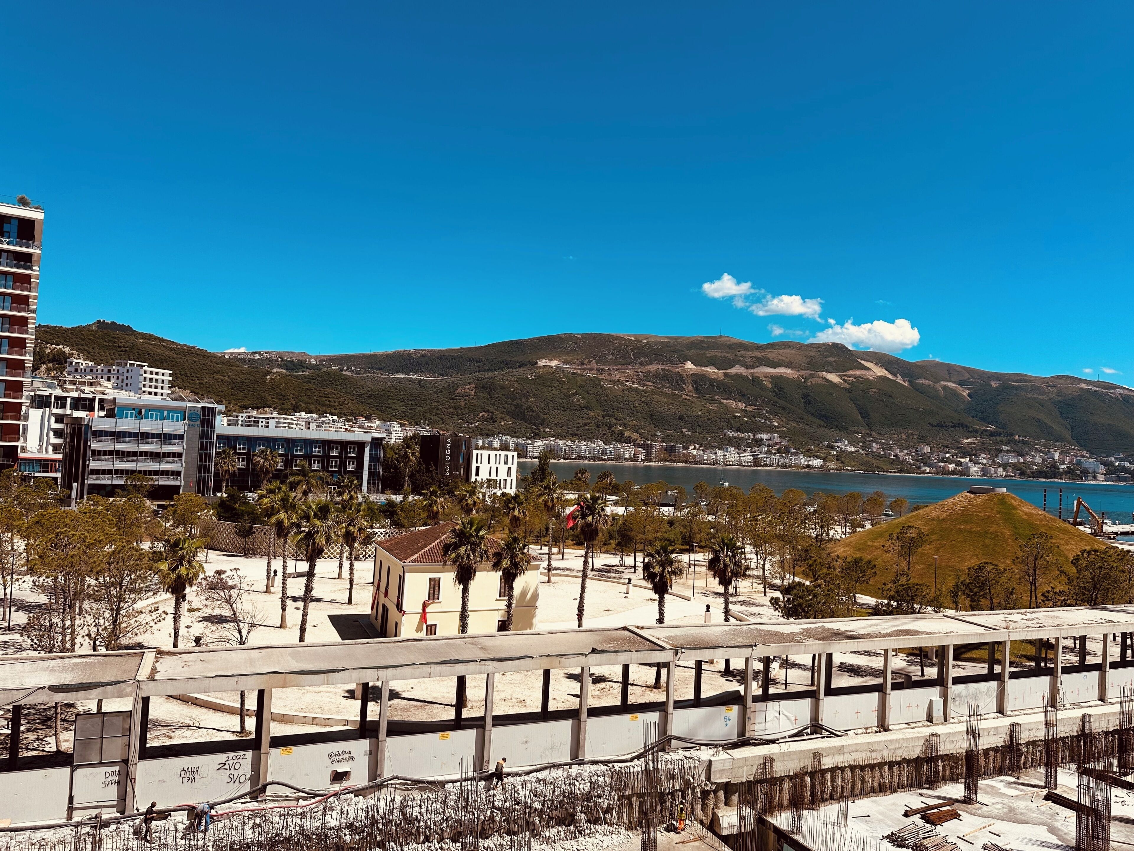 A coastal cityscape with modern buildings, a clear blue sky, and a view of the sea.