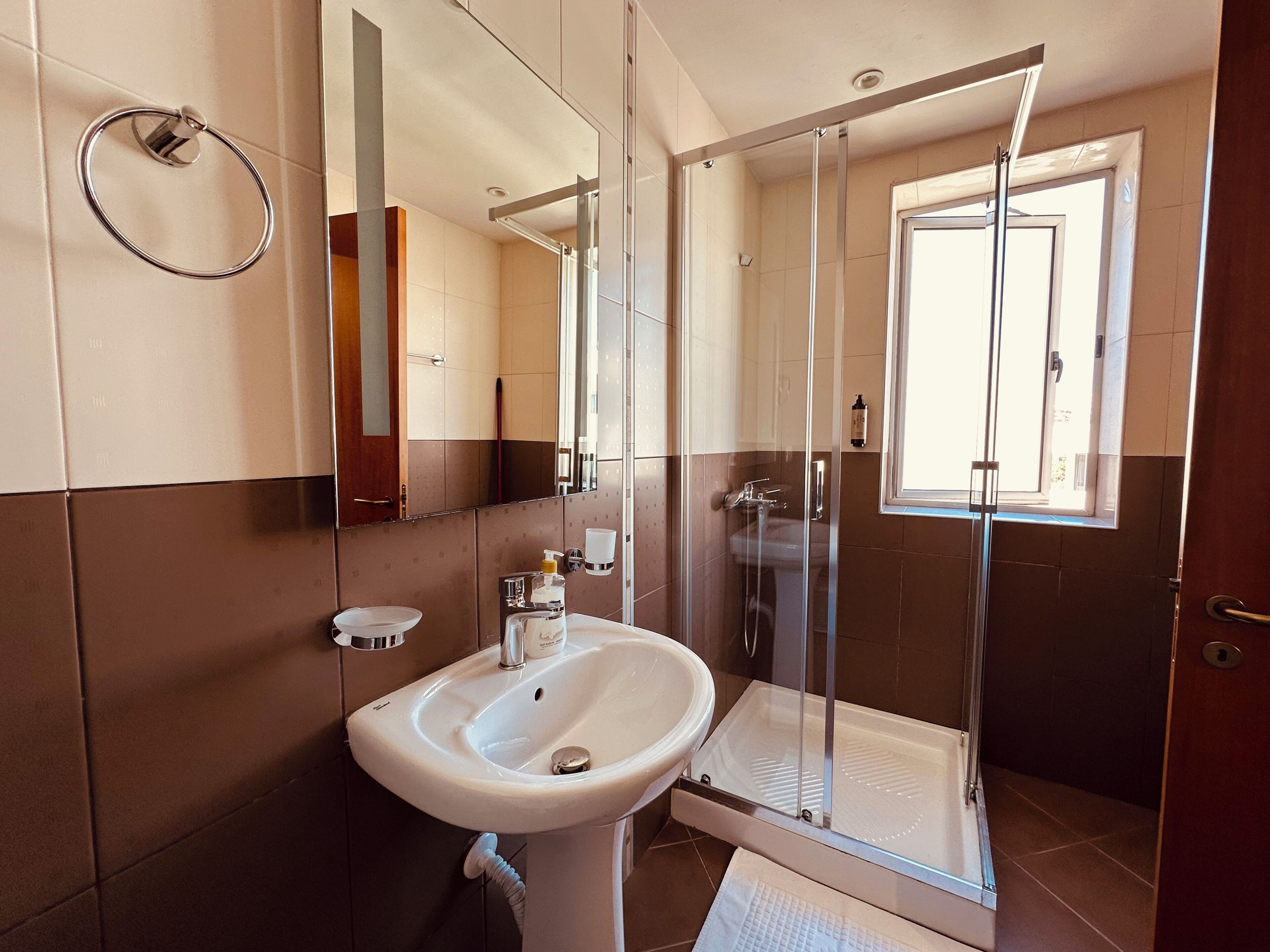 A bathroom with a sink, mirror, shower, and a towel rack.