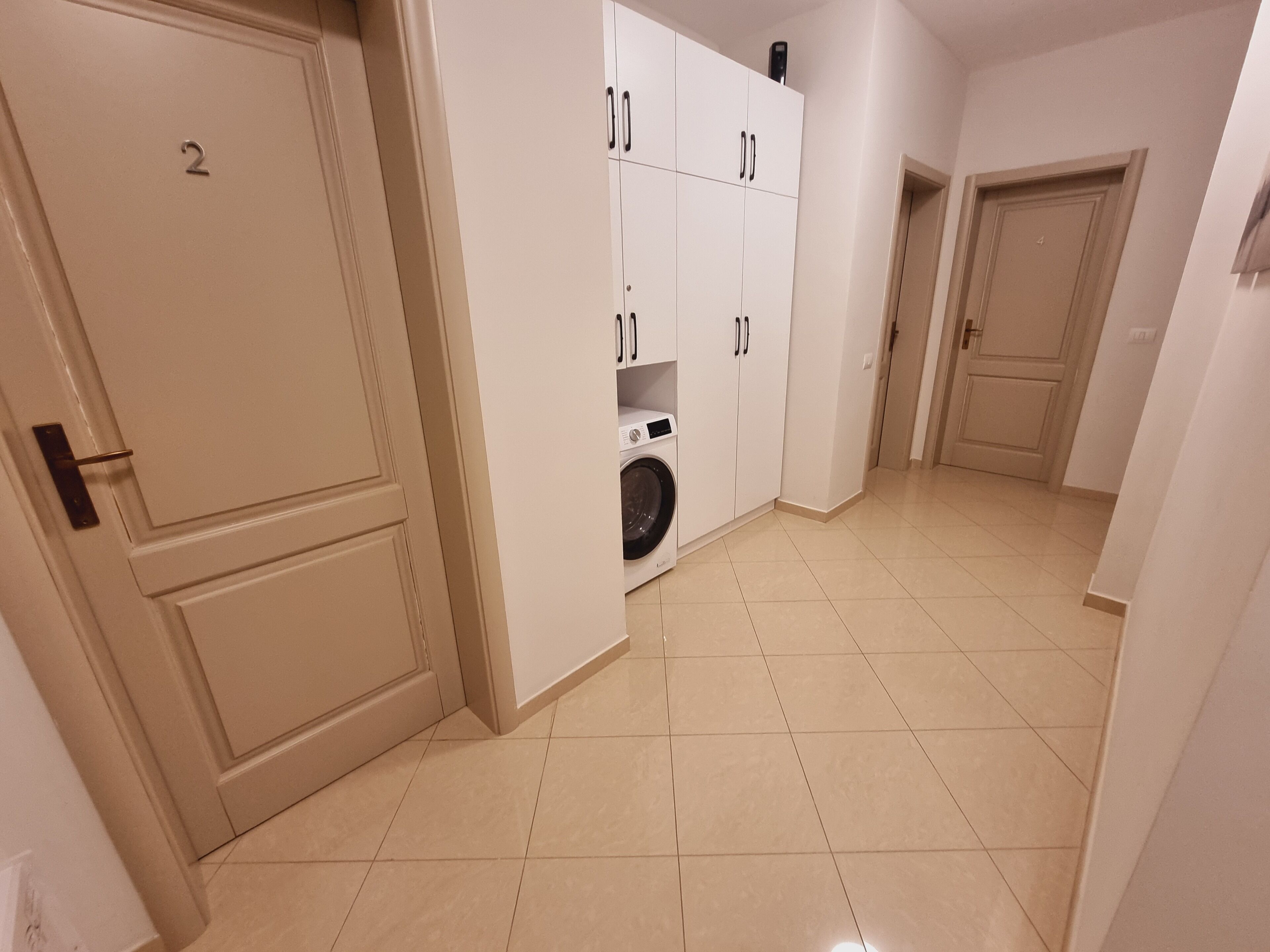 A hallway with a washing machine, white cabinets, and numbered doors.