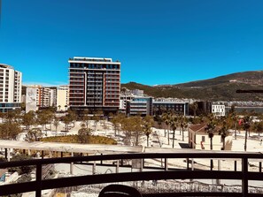 Un complejo moderno de edificios con varios pisos, rodeado de un área ajardinada con árboles y una vista despejada de un paisaje montañoso al fondo.