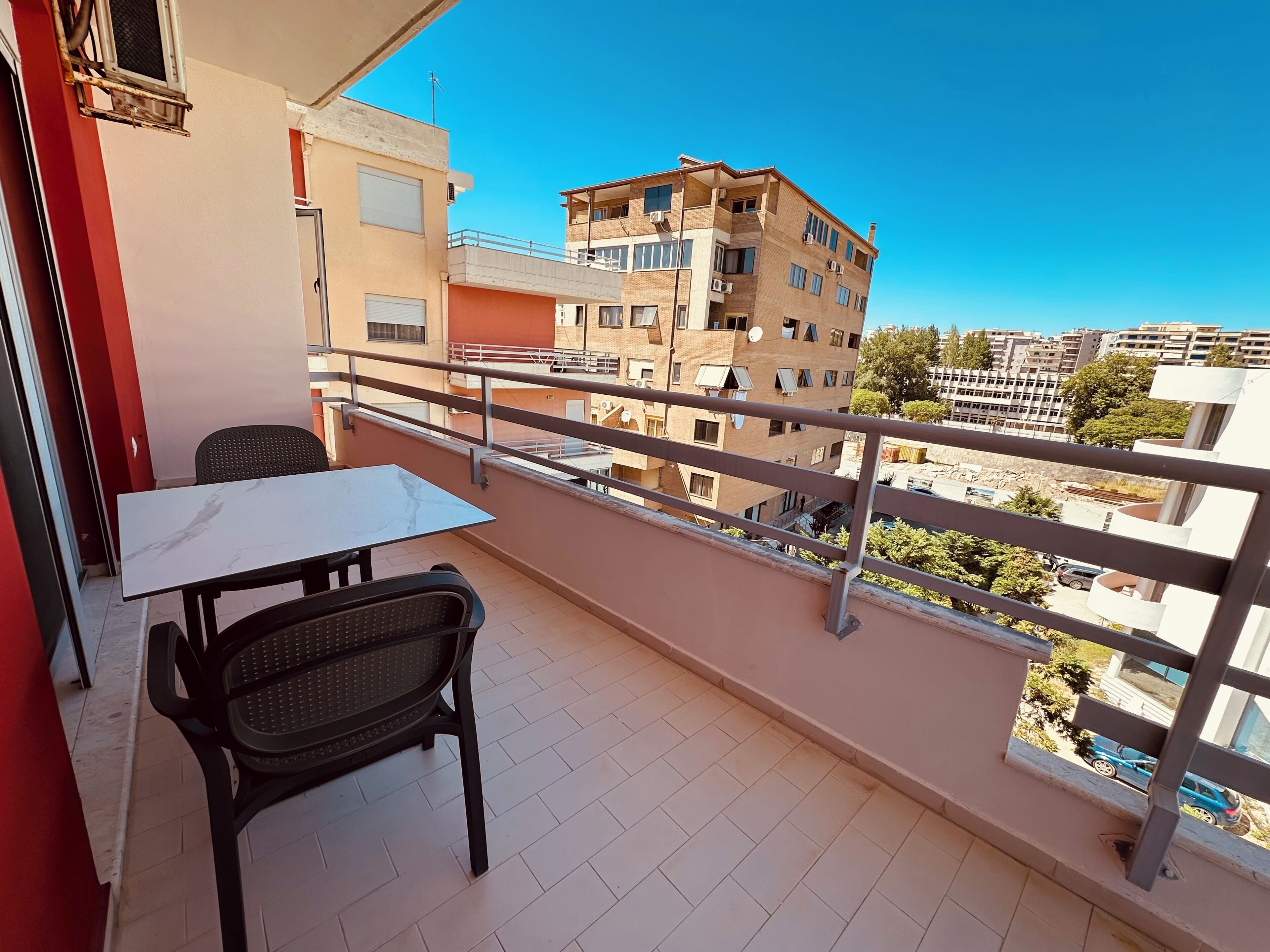 A balcony with a table and chairs, overlooking a residential area with multiple buildings.