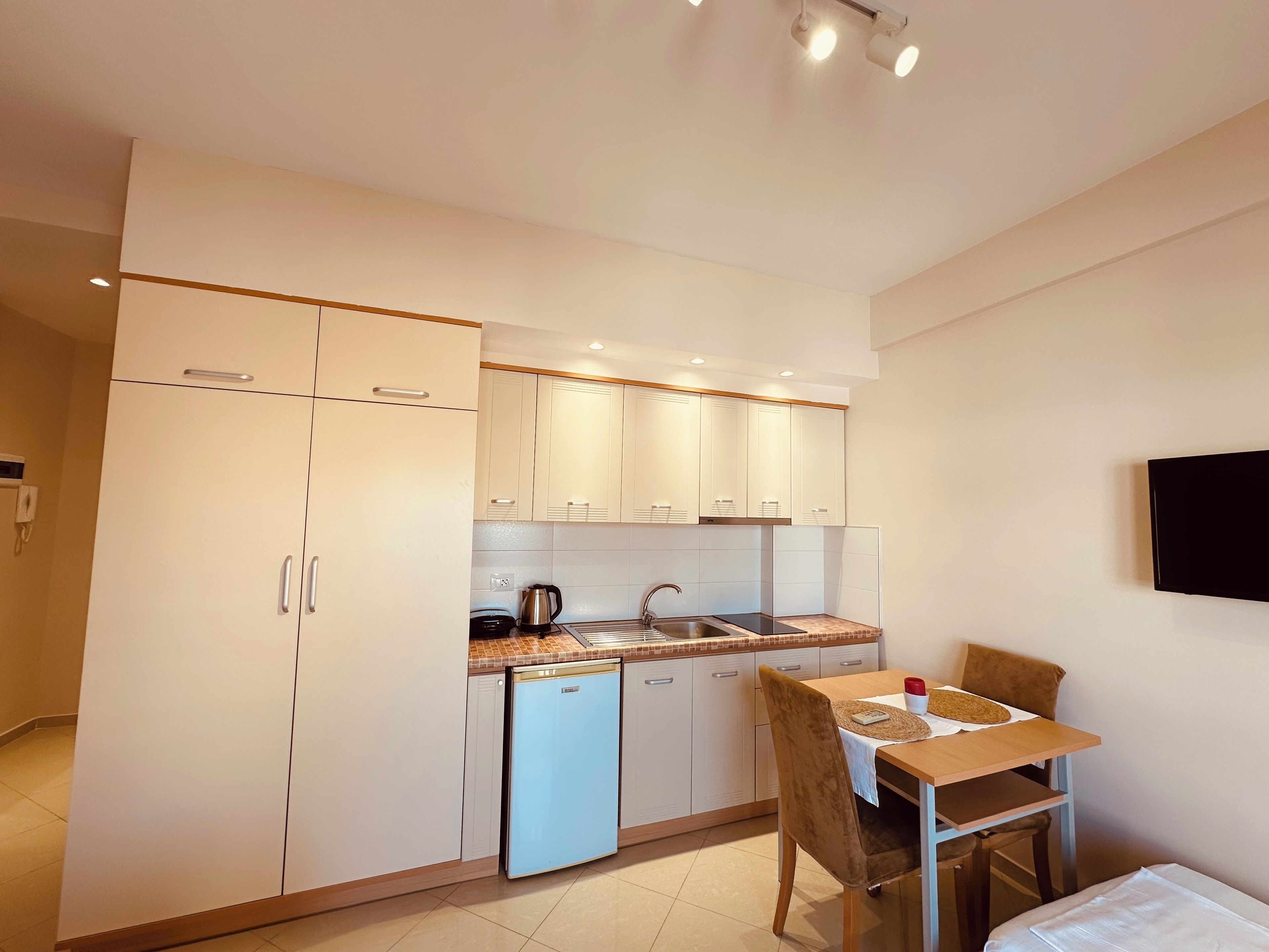 A compact kitchen with a sink, stove, and a small refrigerator. There is a dining area with a table and chairs.