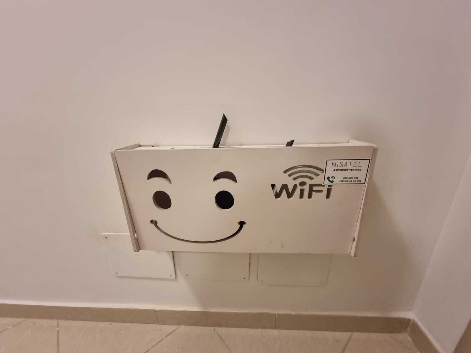 Una scatola elettrica bianca con simbolo WiFi e un'apertura a forma di faccina sorridente, fissata su un muro liscio.