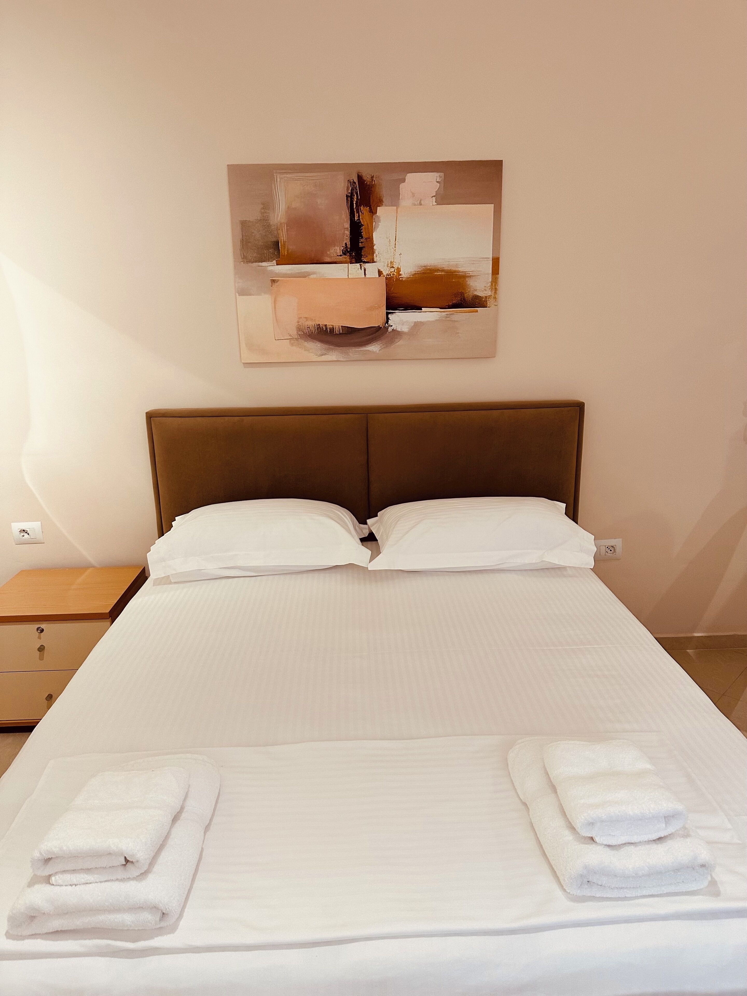 A neatly made bed with white linens and two folded towels at the foot of the bed.
