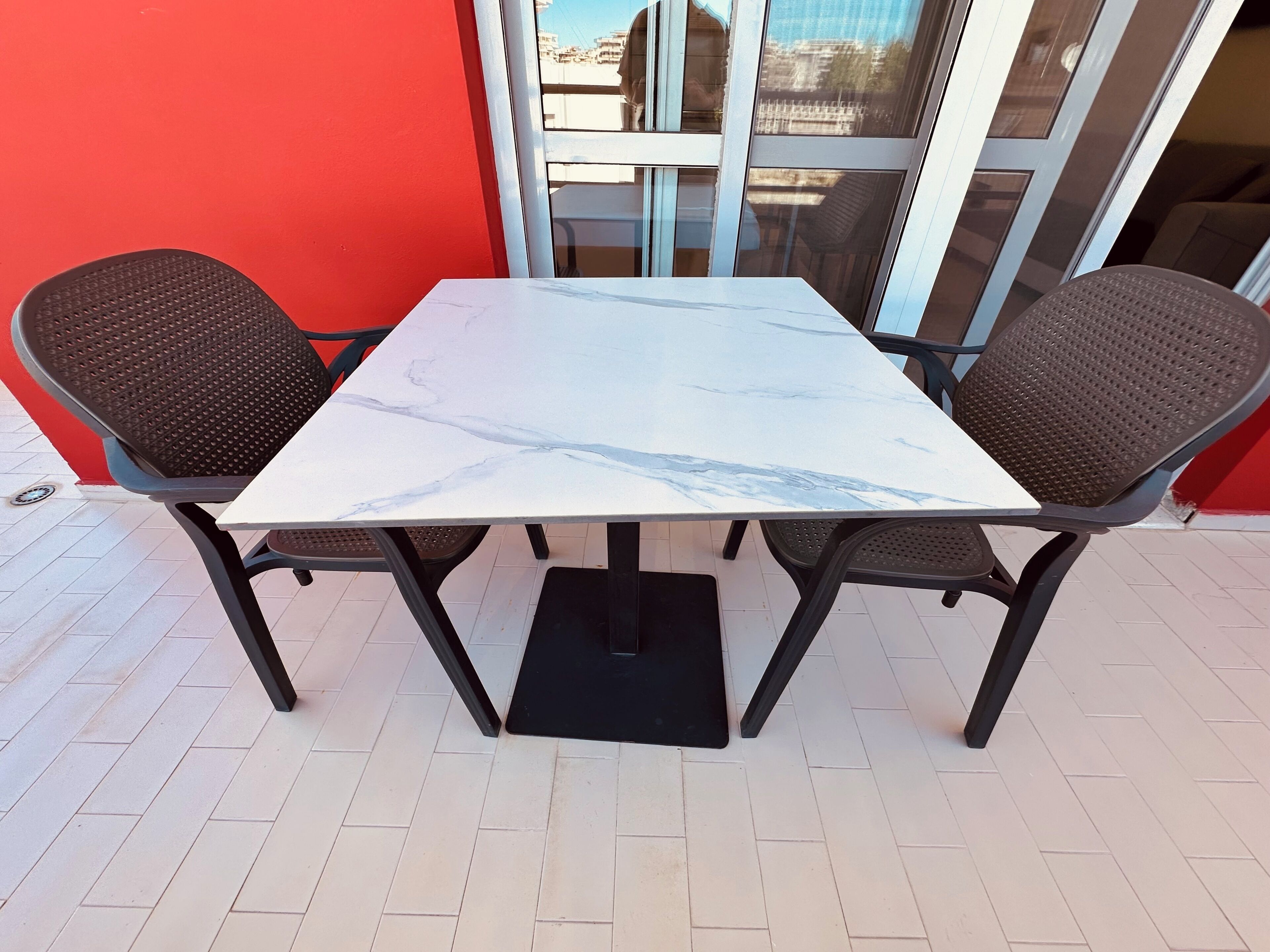 Uma mesa com tampo de mármore branco e duas cadeiras de fibra marrom.