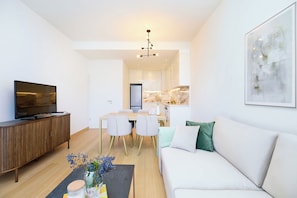 Un salon moderne doté d’un téléviseur à écran plat, d’un meuble en bois, d’un canapé blanc et d’un coin repas avec une table et des chaises.