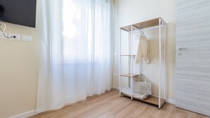 Een kamer met een houten vloer, een witte kledingkast, een kledingrek met een jurk en een handtas, en een aan de muur bevestigde televisie.