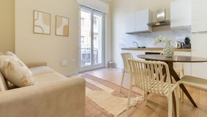 Een moderne woonkamer met een bank, een eettafel met stoelen en een keukenhoek met een fornuis en kasten.